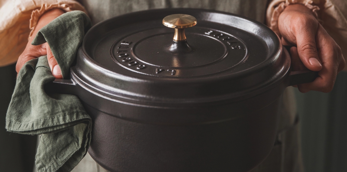 Kädet pitelevät mustaa Staub valurautapataa