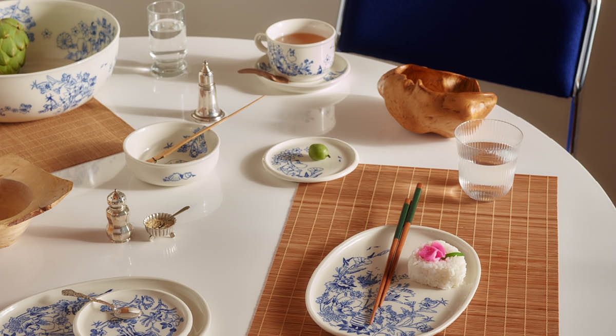 Ett vitt matbord dukat med blå och vita blommiga fat, en kronärtskocka, en risservering med ätpinnar och en cherimoya.