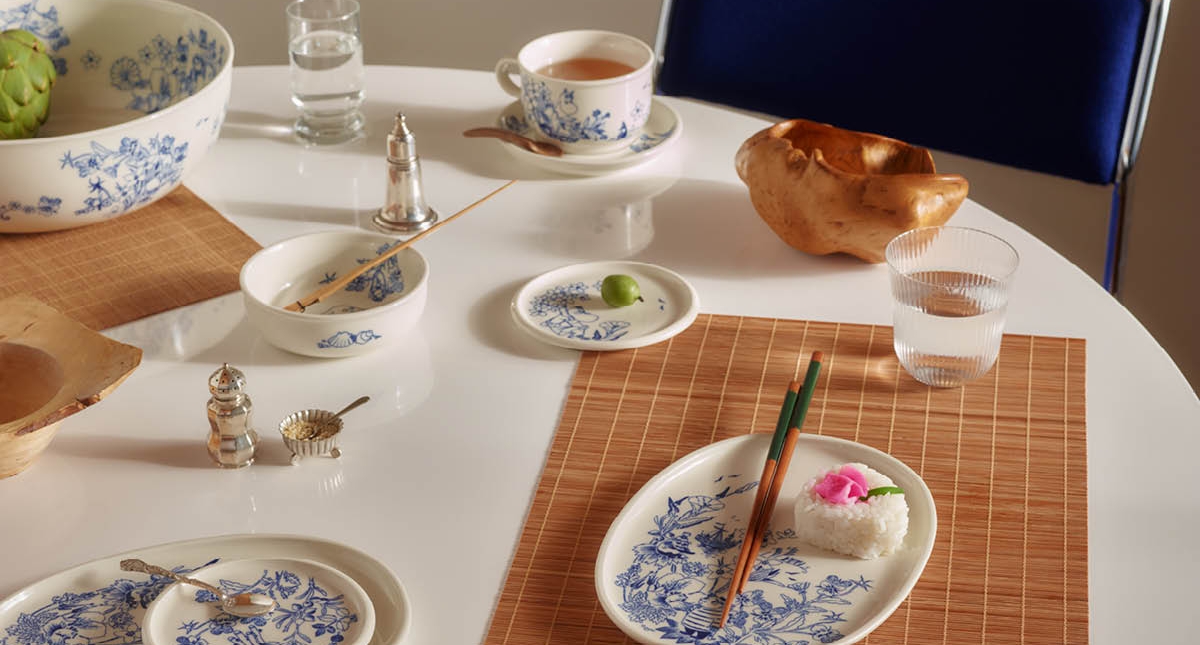 Ett vitt matbord dukat med blå och vita blommiga fat, en kronärtskocka, en risservering med ätpinnar och en cherimoya.