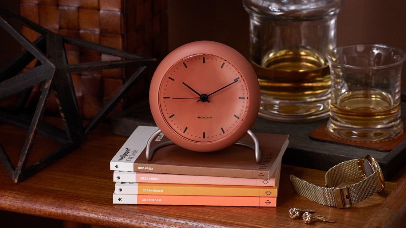 Klockor i orange som står på en hög böcker Arne Jacobsen 