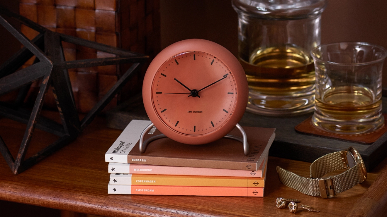 Klockor i orange som står på en hög böcker Arne Jacobsen