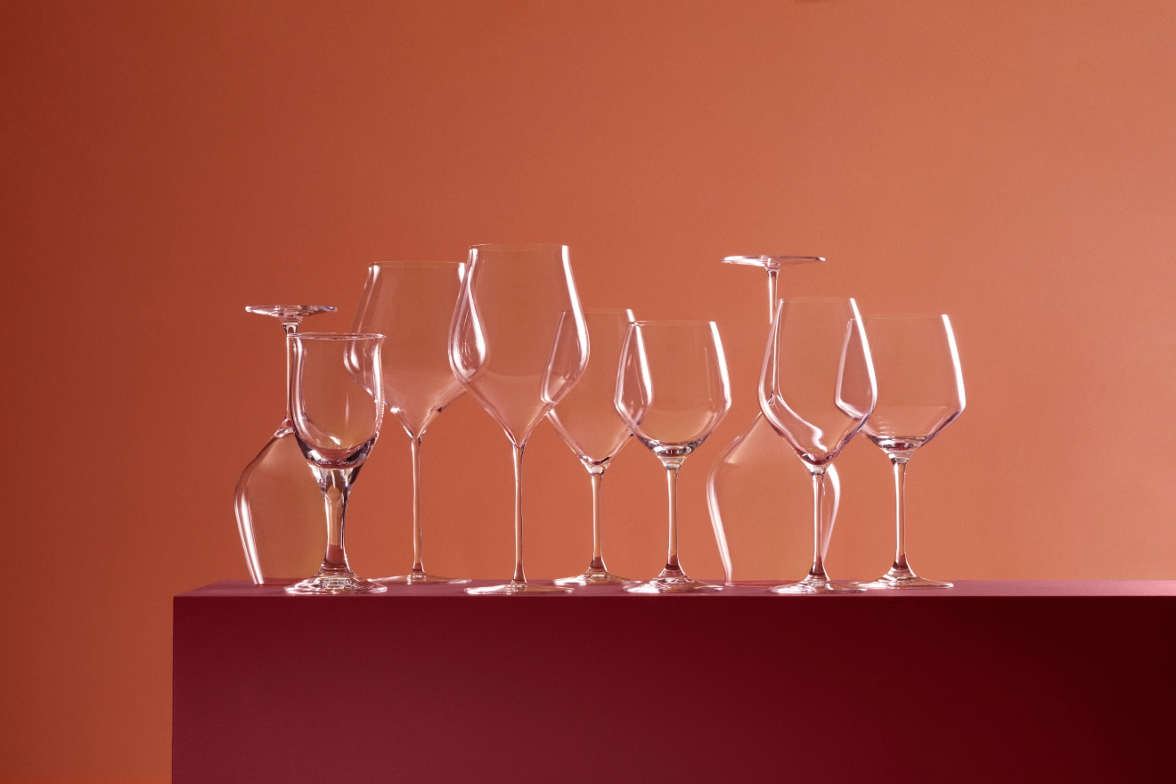 Erilaisia ​​kirkkaita viinilaseja tummanpunaisella tasanteella punertavanruskeaa seinää vasten.