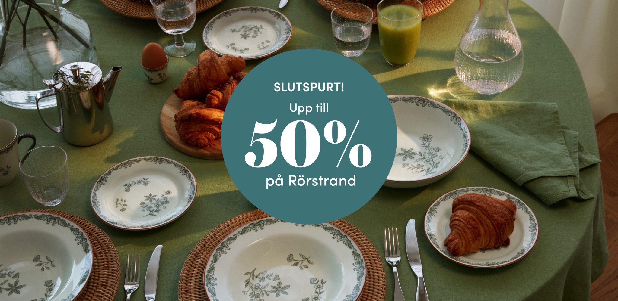 Grön frukostdukning med blommigt Rörstrandsporslin och croissanter samt erbjudandet ”Slutspurt – upp till 50 % på Rörstrand” i mitten.