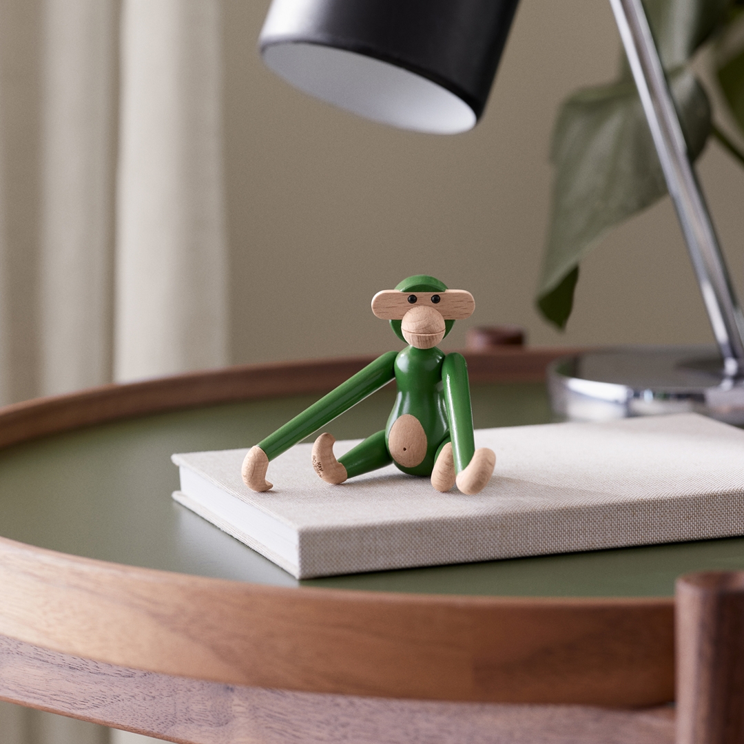 En grön träapafigur sitter på en bok på ett grönt bord.