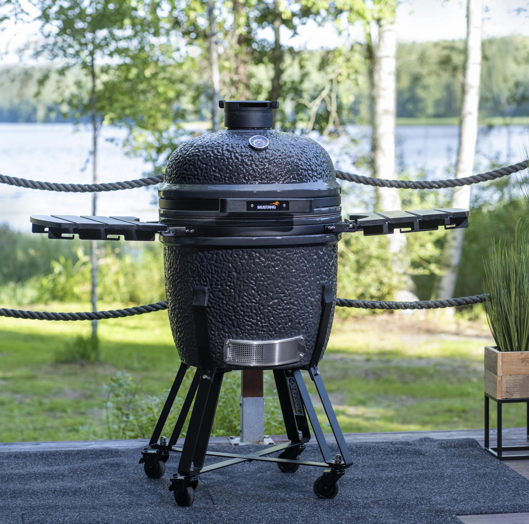 Textured dark gray kamado grill with side tables on a deck overlooking a lake.