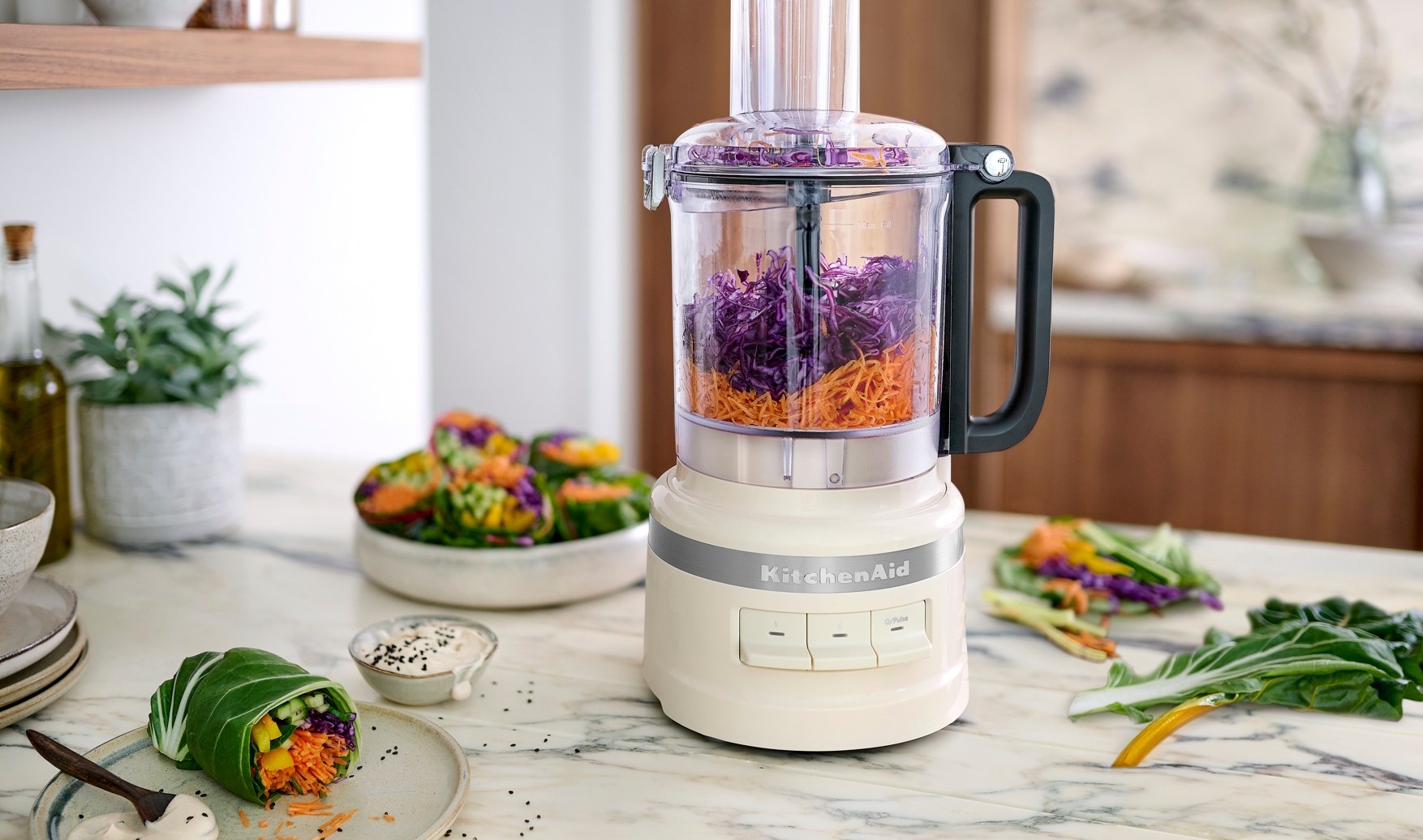 Matberedare från KitchenAid som river morötter och rödkål på ett marmorbord i ett modernt kök.