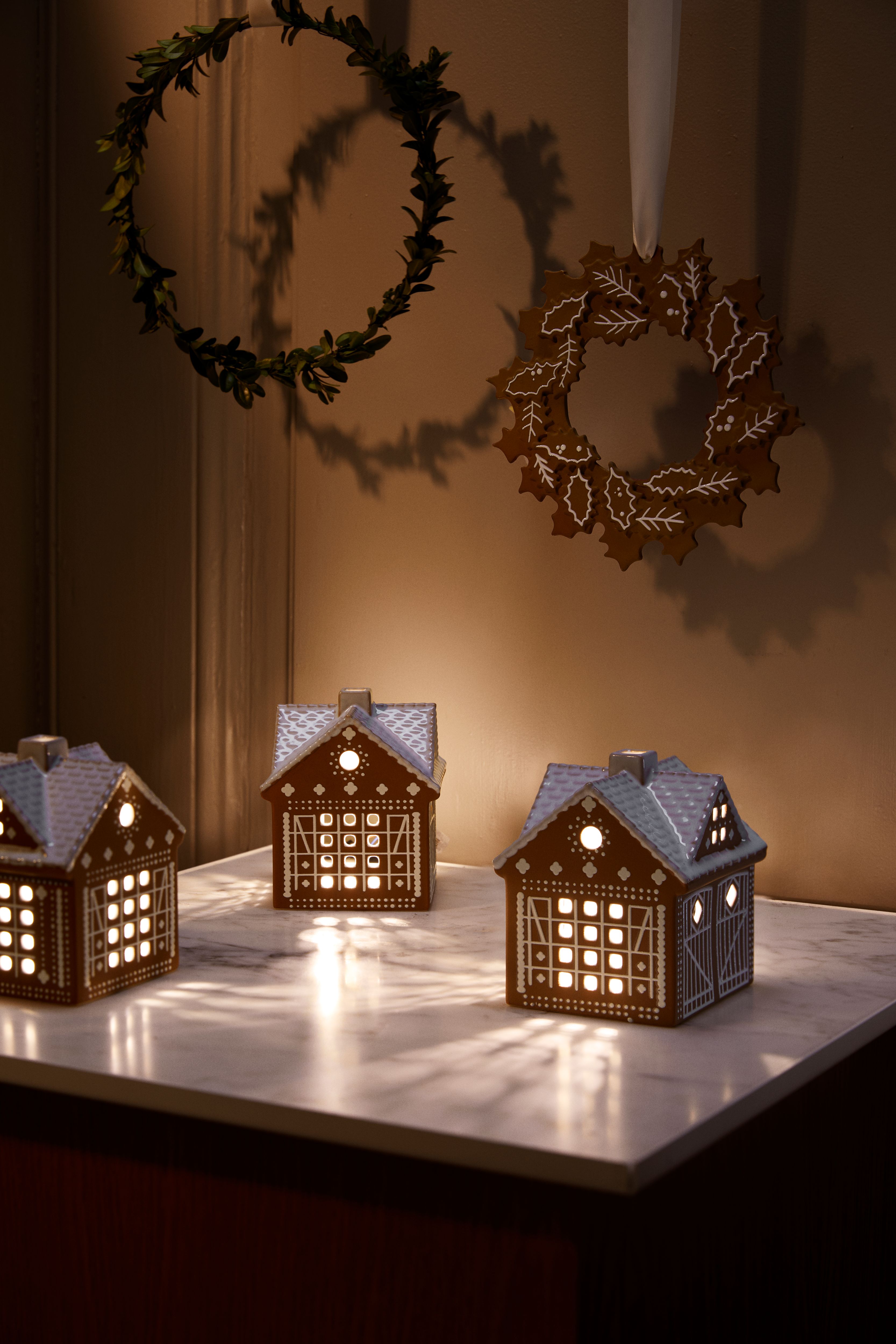 3 lyslykter i form av pepperkakehus som står på et bord og lyser opp et mørkt rom