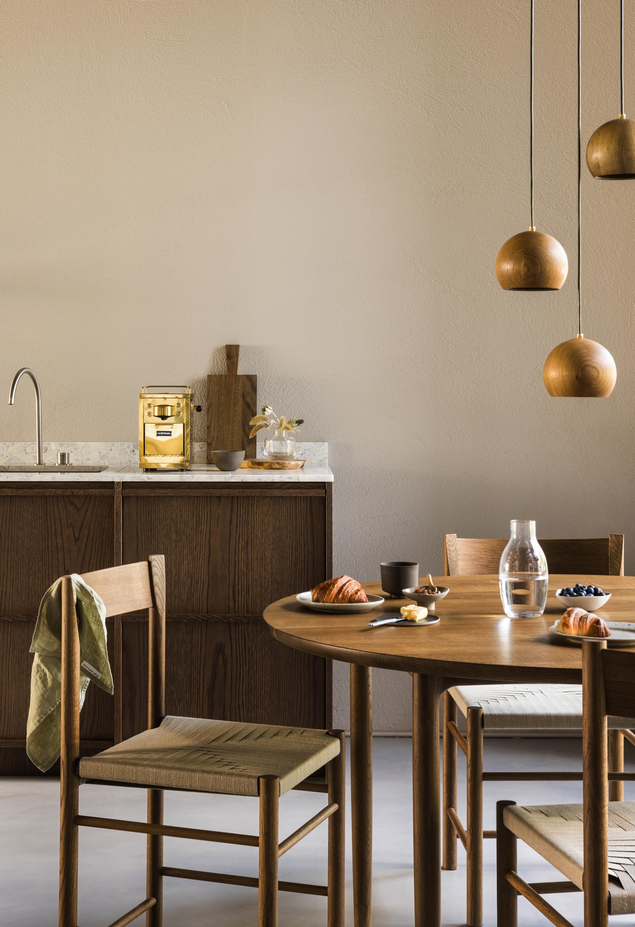 Kök i bakgrunden med fokus på ett runt träbord och tre stolar i rotting