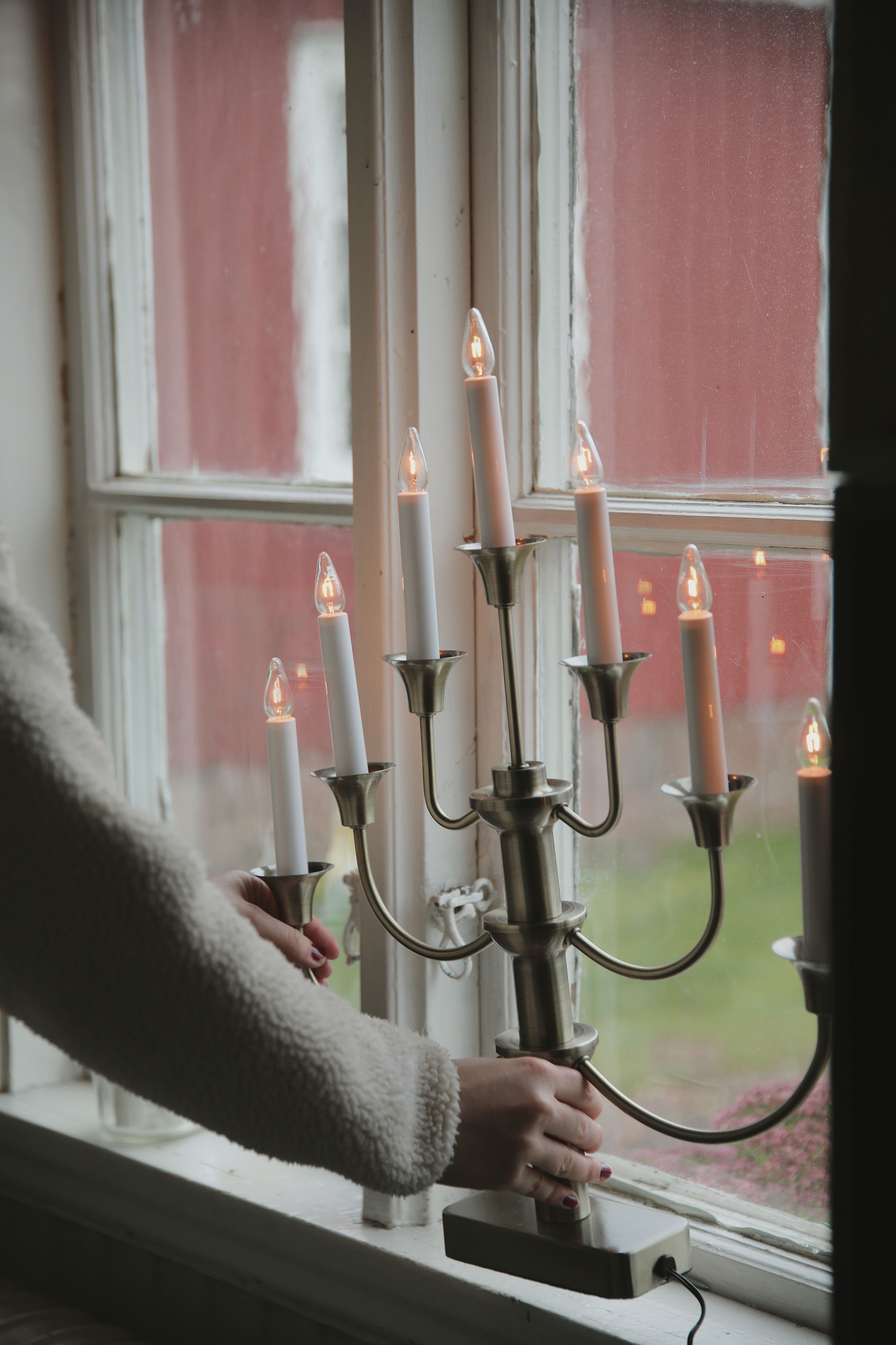 En person placerar en tänd elektrisk adventsljusstake i ett fönster.