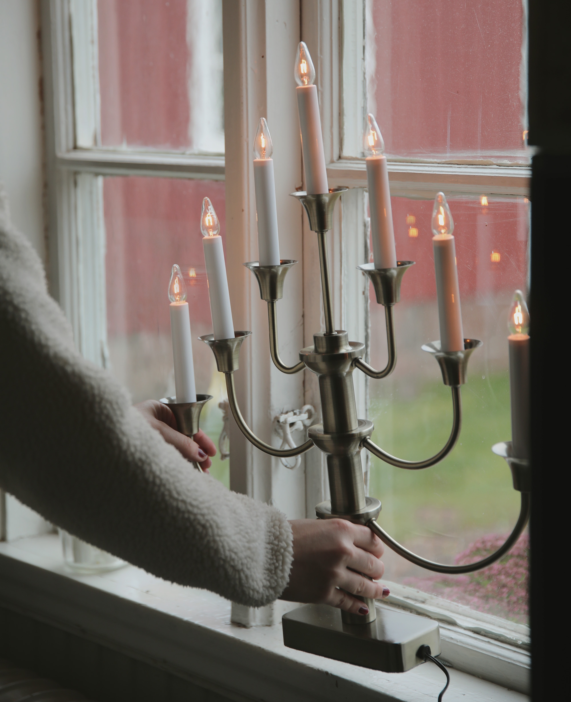 En person placerar en tänd elektrisk adventsljusstake i ett fönster.