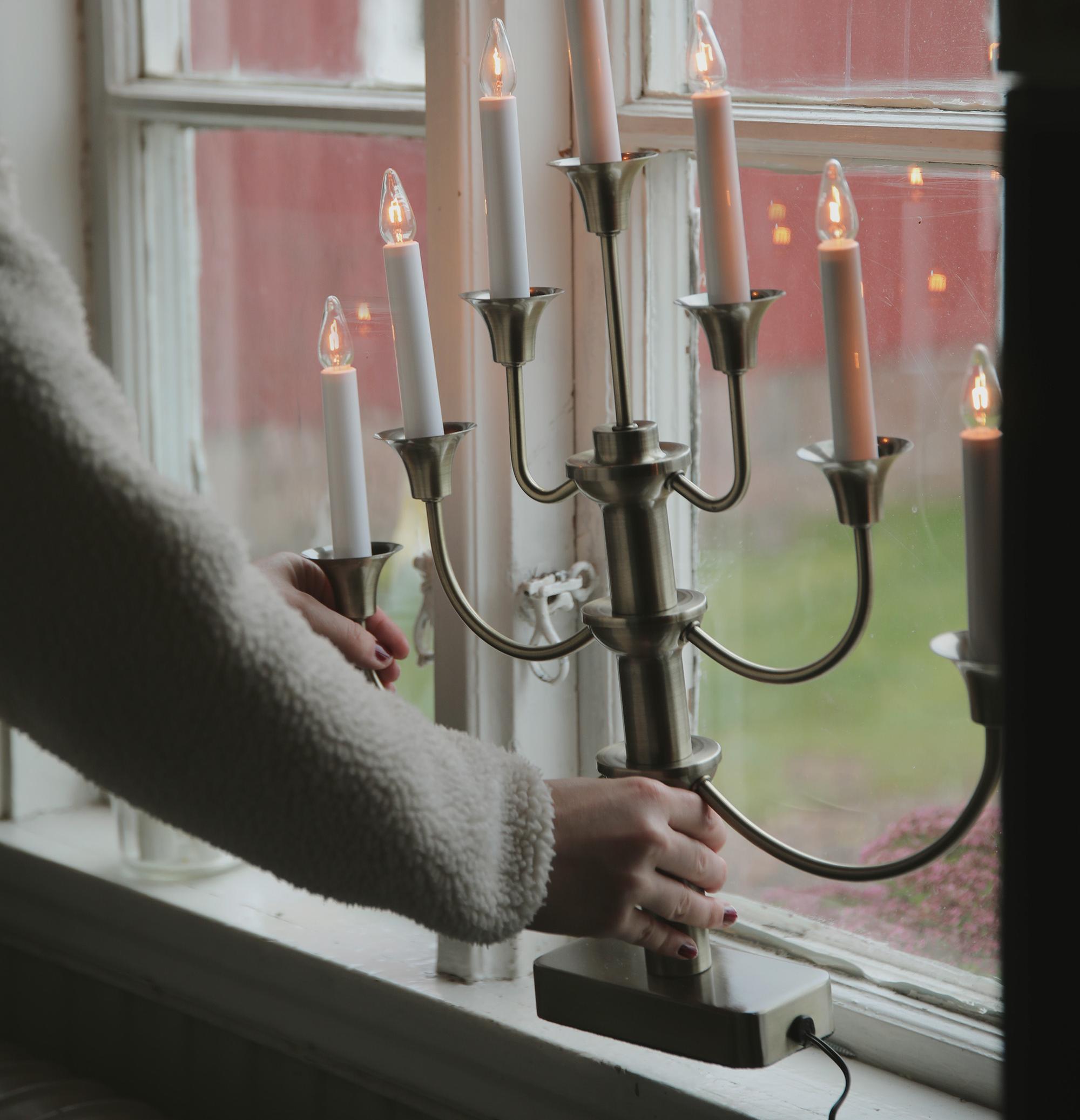 En person placerar en tänd elektrisk adventsljusstake i ett fönster.