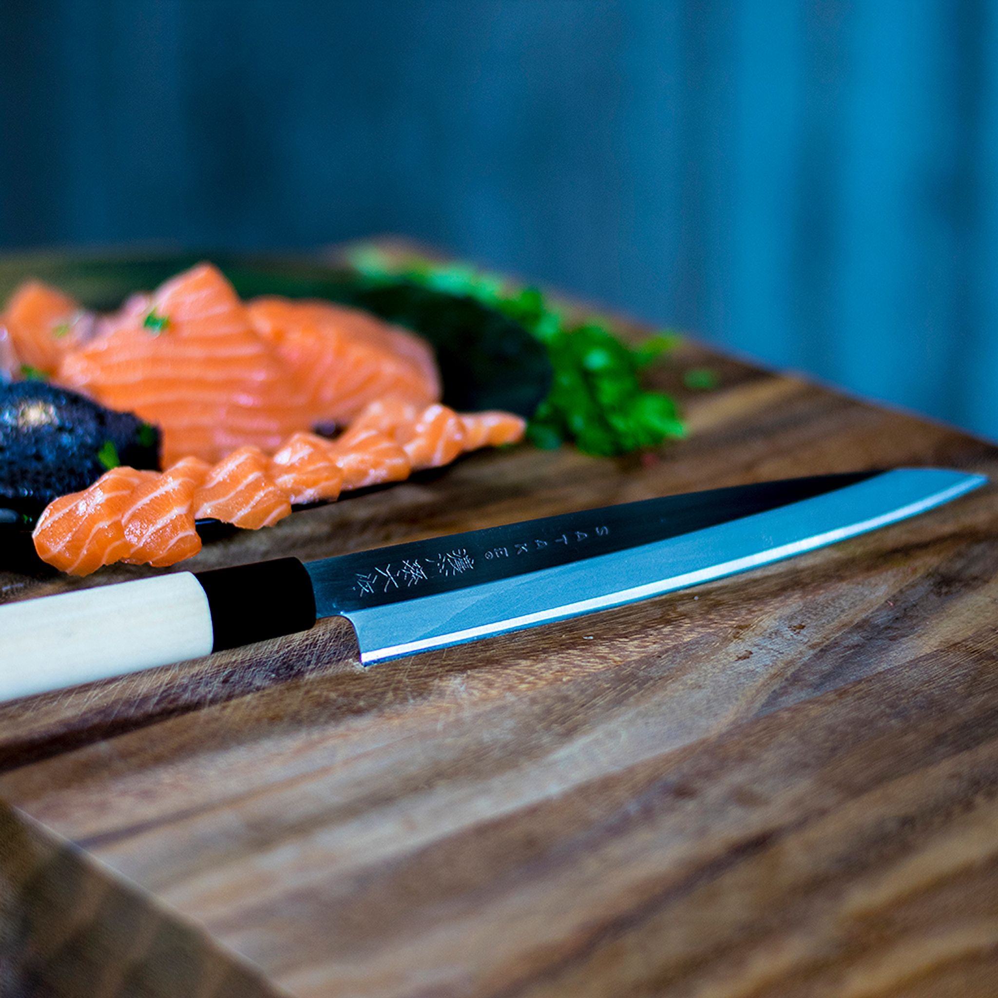 Japansk kockkniv bredvid skivad lax och gröna örter på en skärbräda.