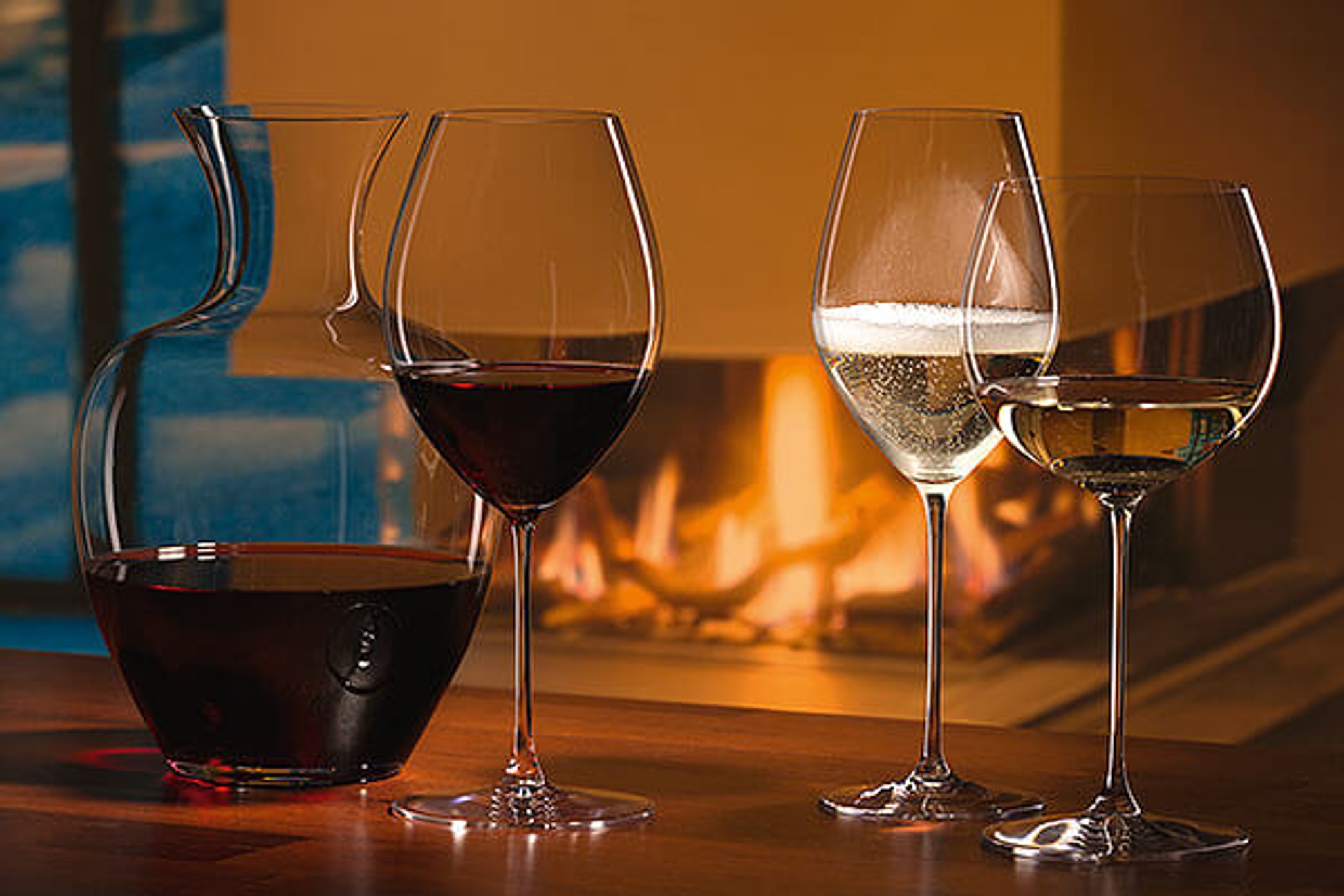 Vinglas med rött och vitt vin samt en karaff framför en stämningsfull öppen spis.