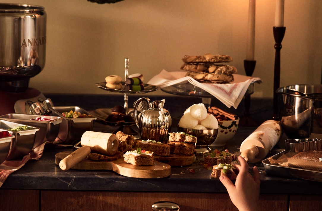Ett barn sträcker sig efter julgodis på ett stämningsfullt köksbord med bakning, tända ljus och juldekorationer.