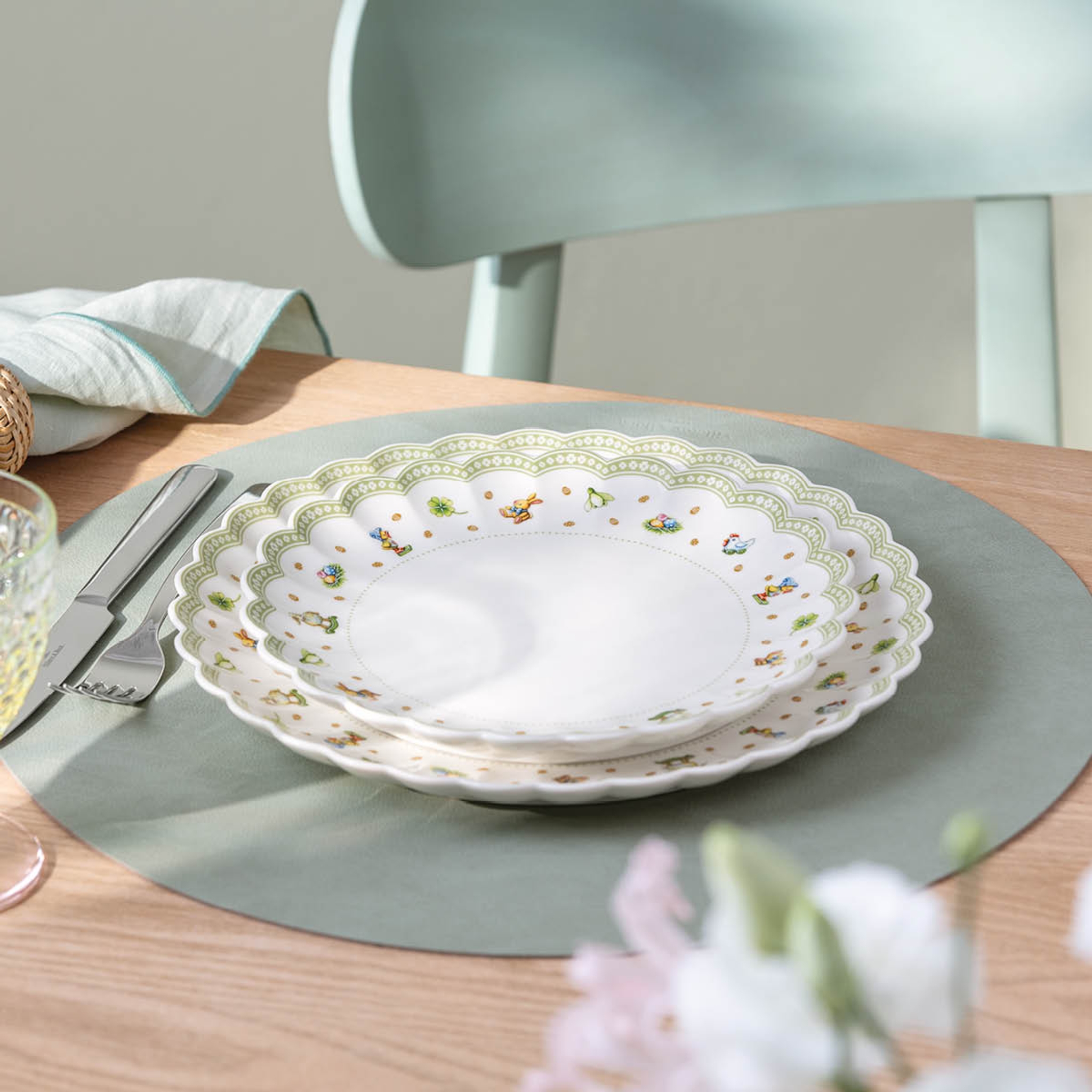 Pinottuja valkoisia lautasia, joissa on simpukankuoria ja vihreäkuvioisia reunoja sekä pieniä eläinkuvia, salvianvihreällä tabletilla.