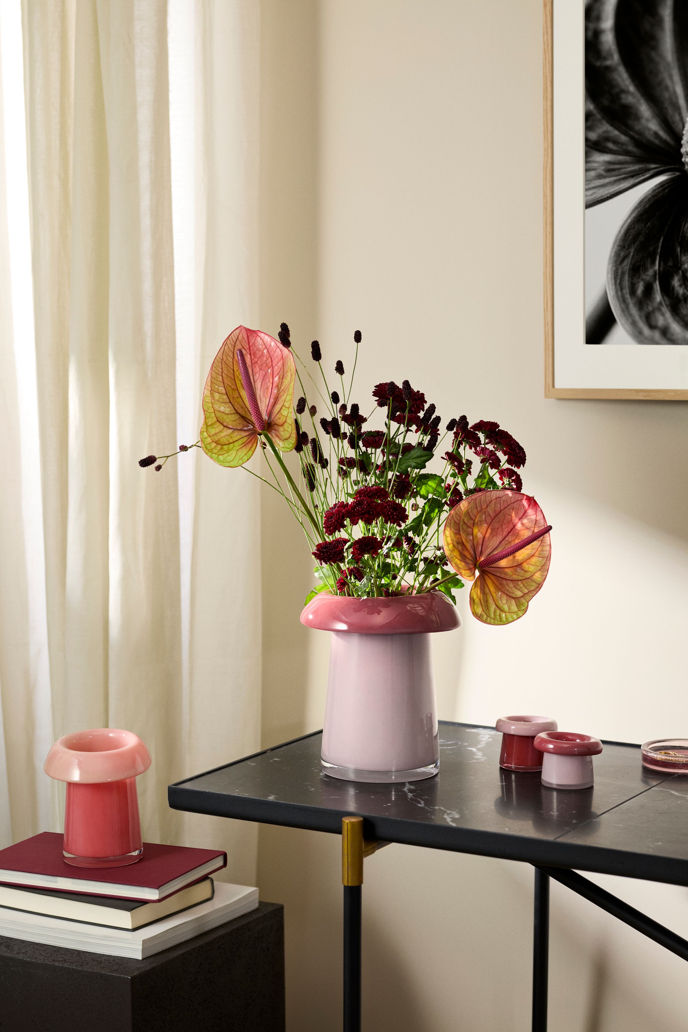 Rosa vas med anthurium och mörkröda blommor på ett svart bord i ett ljust, modernt rum.