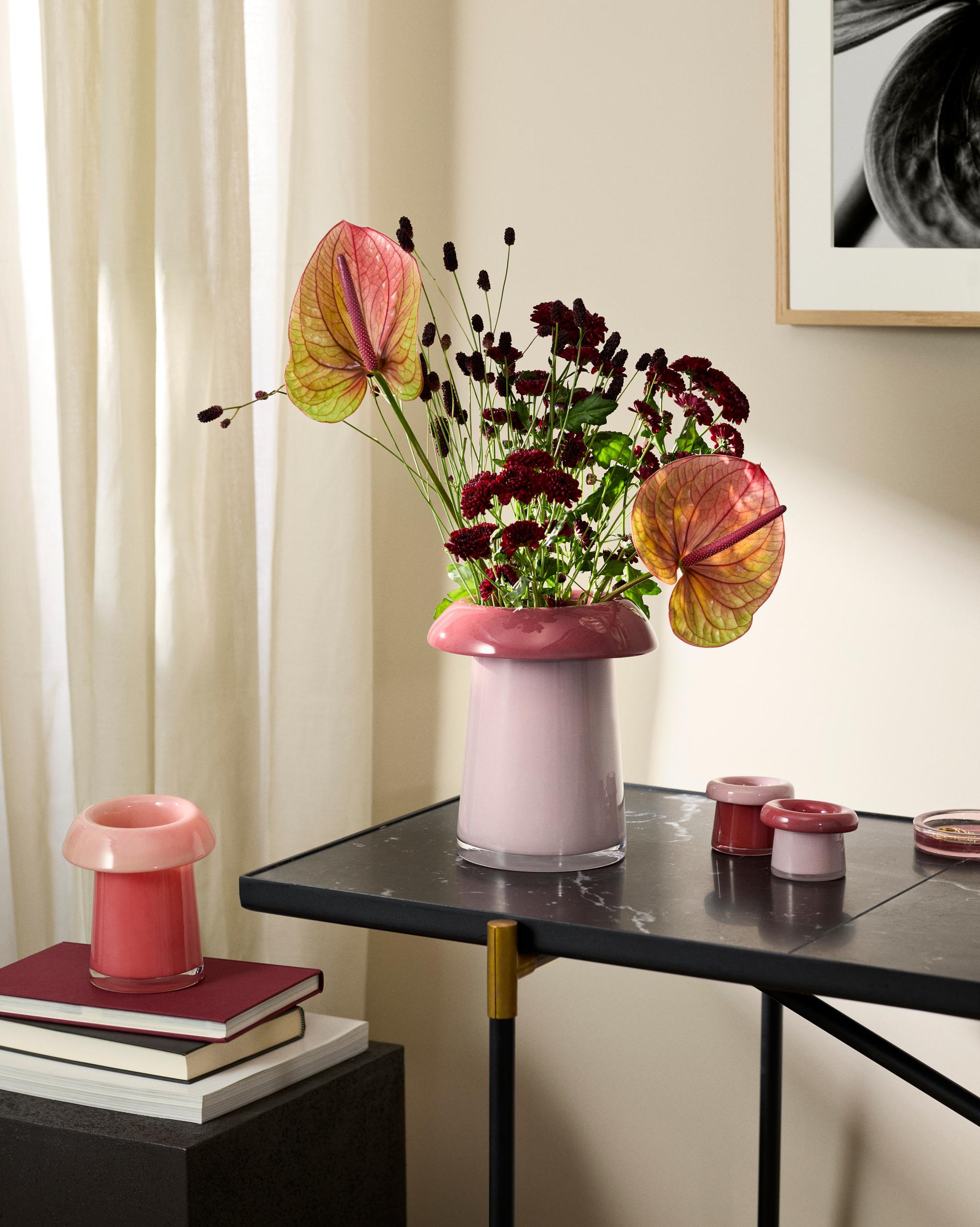 Rosa vas med anthurium och mörkröda blommor på ett svart bord i ett ljust, modernt rum.