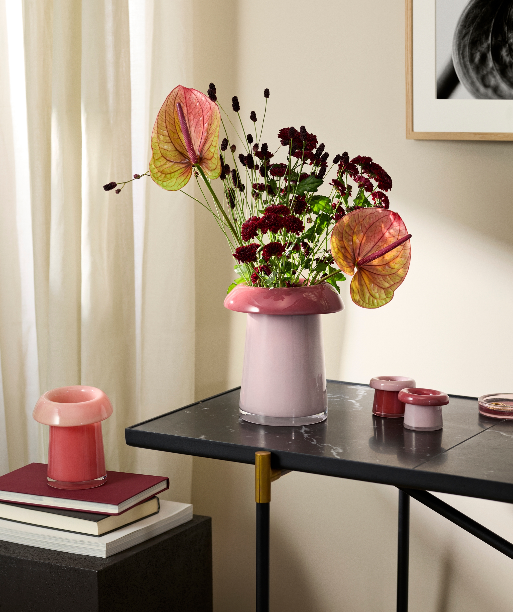 Rosa glasvas med en färgstark bukett av anthurium och mörkröda blommor på ett svart marmorbord.