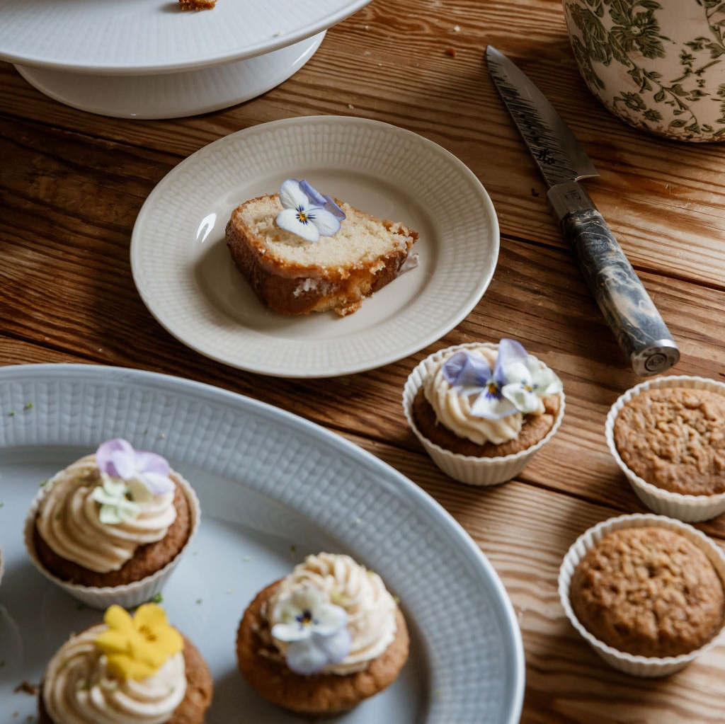 Sockerkaka och cupcakes dekorerade med ätbara violer står uppdukade på ett rustikt träbord.