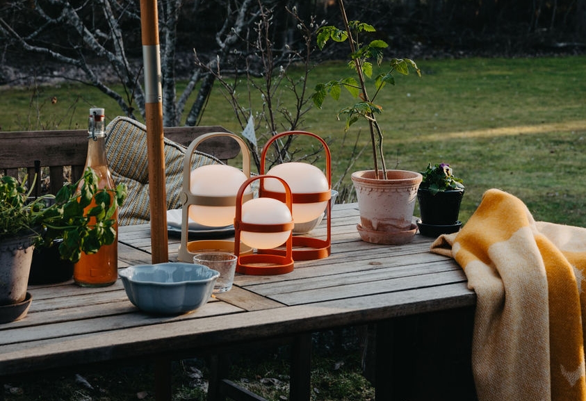 Tre glødende bærbare lykter og et gult teppe på et utendørs trebord