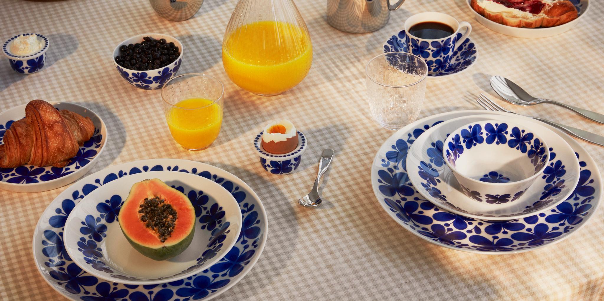 Uppdukat frukostbord med blåvitt porslin, croissanter, papaya, ägg, kaffe och apelsinjuice.