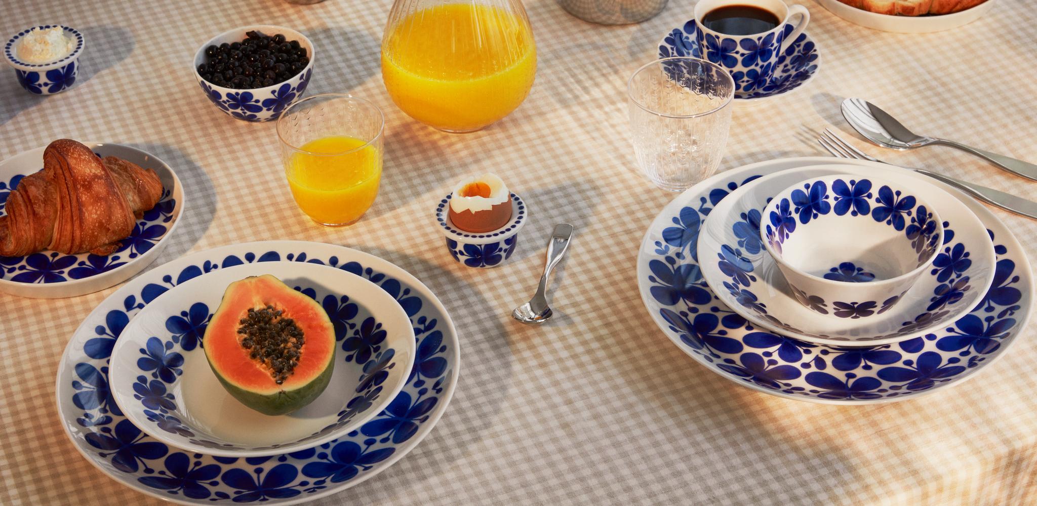 Frokostbord dekket med blåmønstret servise, croissanter, papaya, egg, kaffe og appelsinjuice.