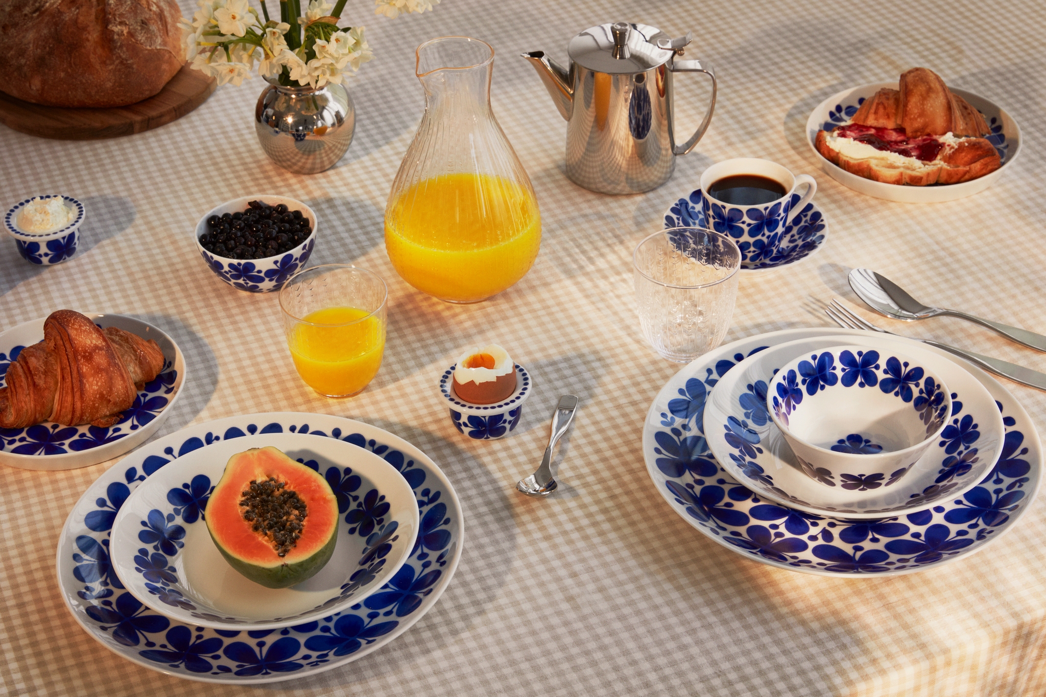 Uppdukat frukostbord med blåvitt porslin, croissanter, papaya, ägg, kaffe och apelsinjuice.