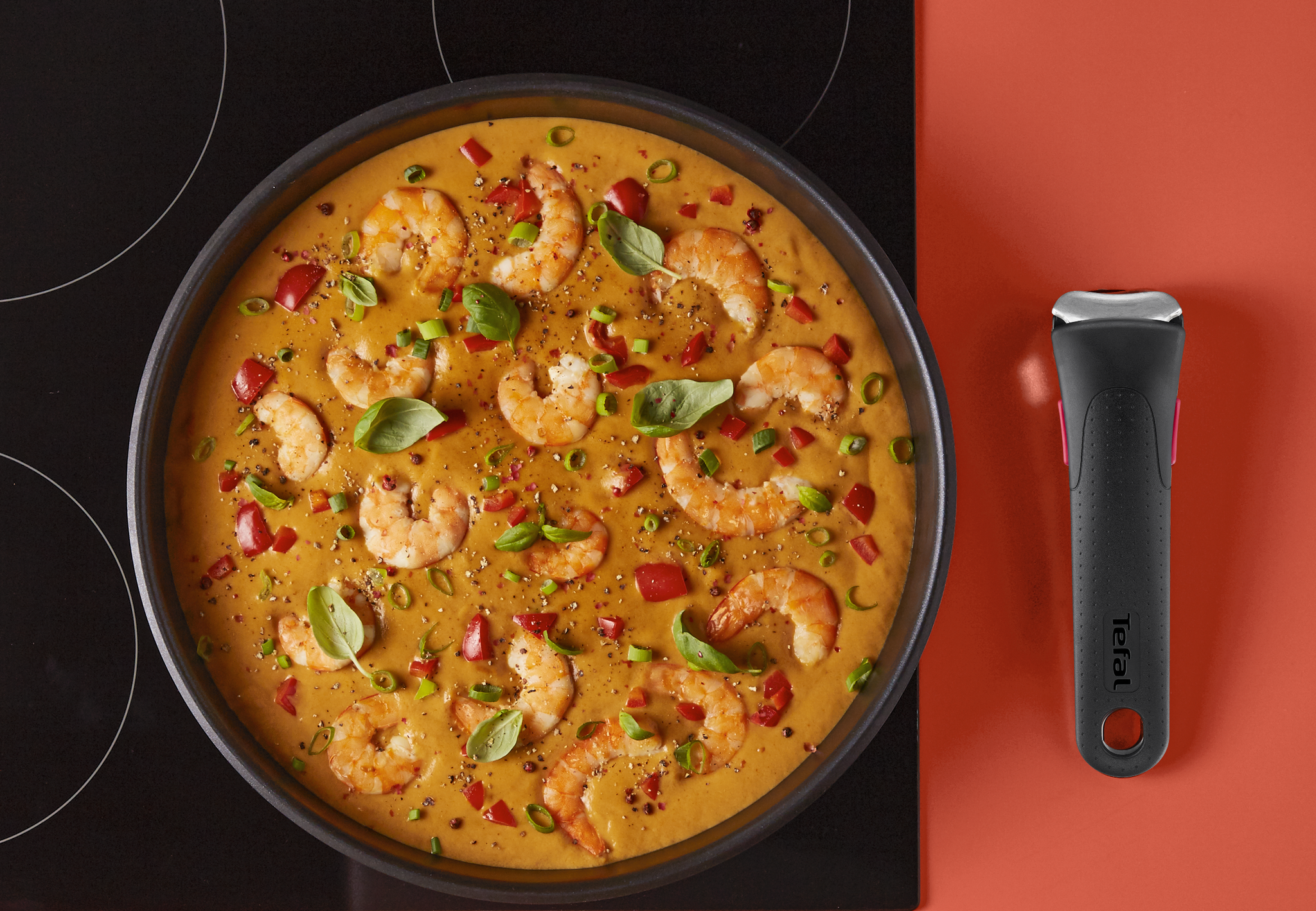 Krämig räkrätt med paprika och örter i stekpanna på spishäll, omgiven av kryddor och ingredienser.