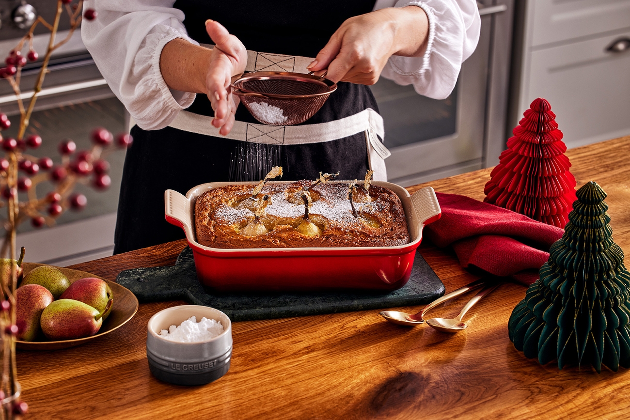 En person som strör florsocker över en kaka i en ugnsform