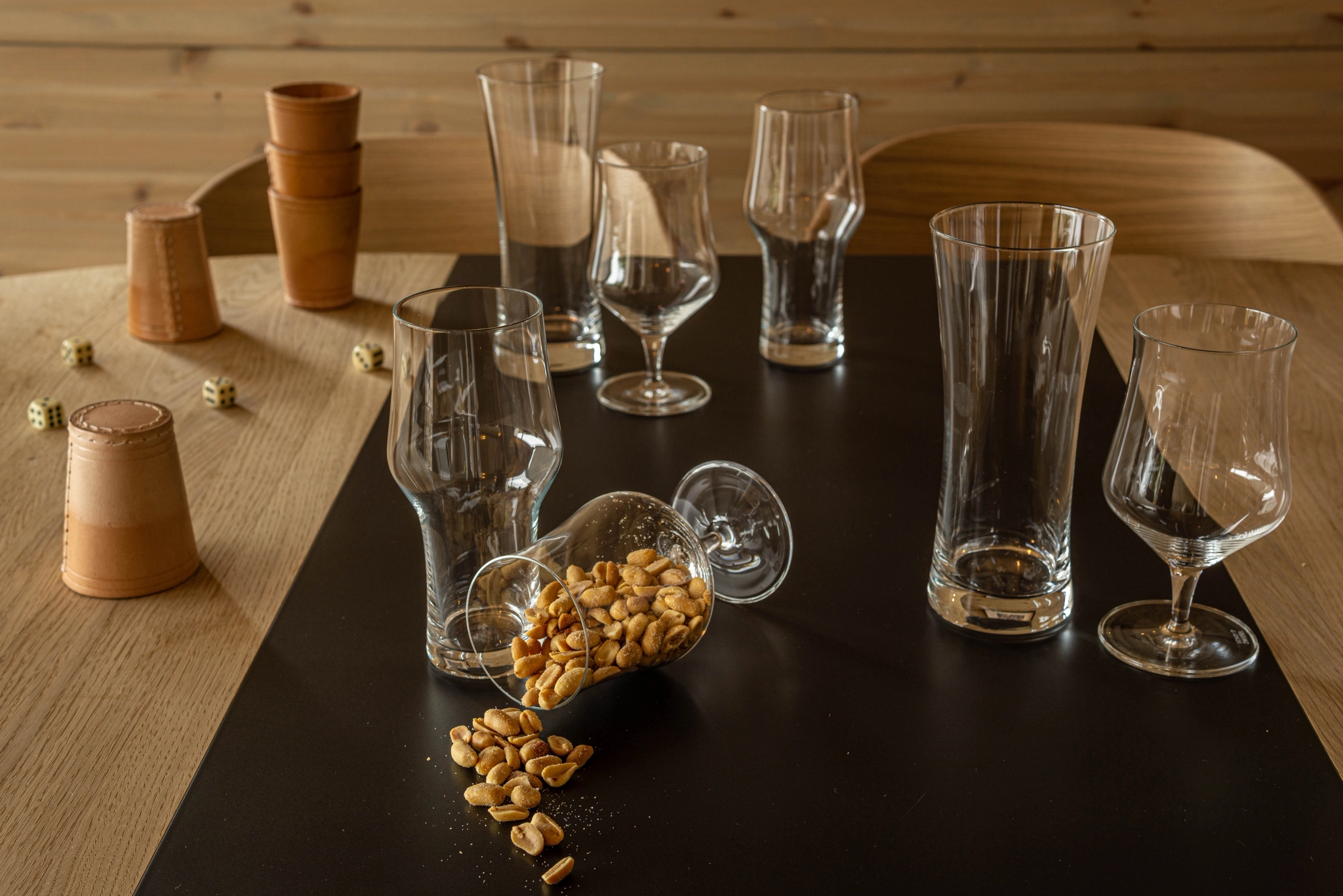 Tomma ölglas och tärningsmuggar står på ett bord där ett glas vält och salta jordnötter har spillts ut.