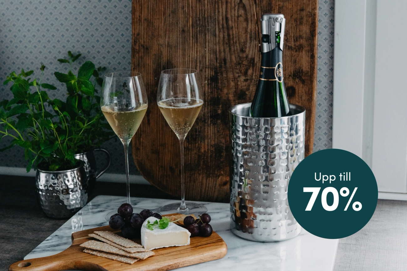  Två champagneglas, en flaska i en hamrad vinkylare, ost, kex och vindruvor på en marmoryta