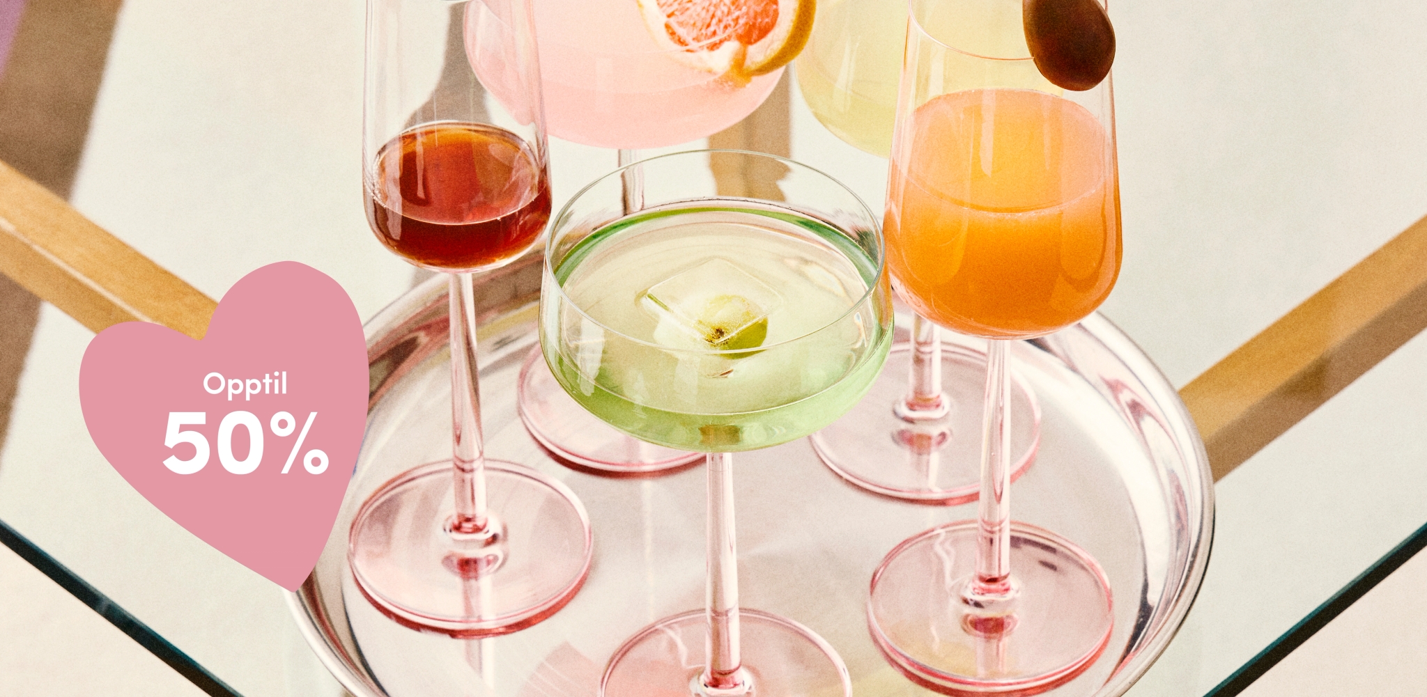 Fem fargerike cocktailer i elegante glass med rosa stilk på et sølvfat, med et rosa hjertegrafikk med teksten «Opptil 50 %».