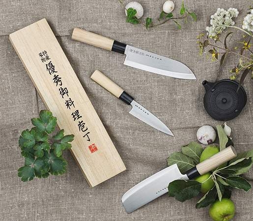 Japanilaiset keittiöveitset puisine kahvoineen aseteltuna luonnonmateriaalien ja yrttien kanssa rustiikkiselle pellavakankaalle.