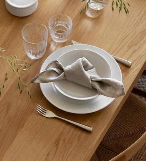 Lyst skandinavisk spiserom med et elegant dekket spisebord i tre, naturfargede stoler og en stor pendellampe.
