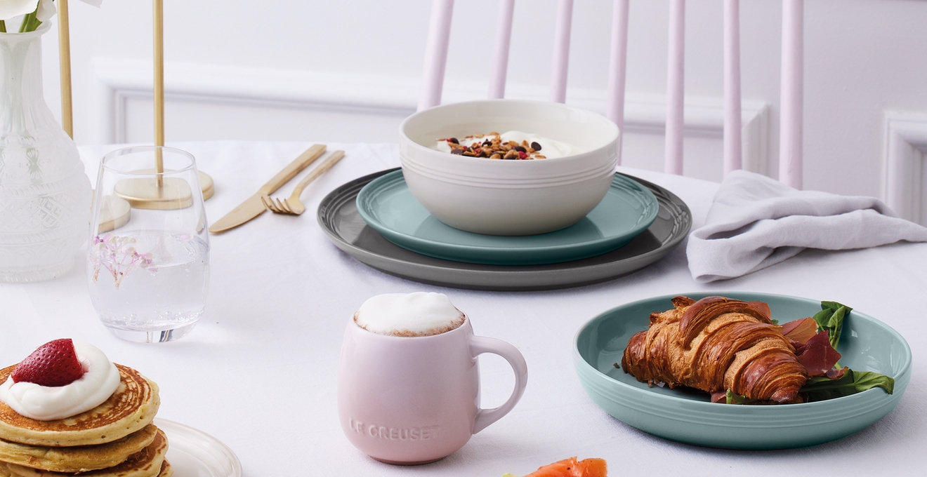 En ljus frukost med pannkakor med jordgubbar, bagels med lax och avokado, en croissant och yoghurt, serverad på pastell- och neutralfärgade fat.