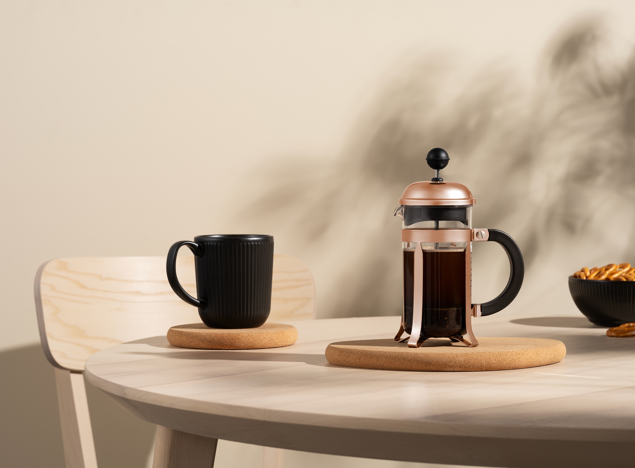 Stilren kaffepress i koppar med svart mugg på ljust träbord i minimalistisk köksmiljö.