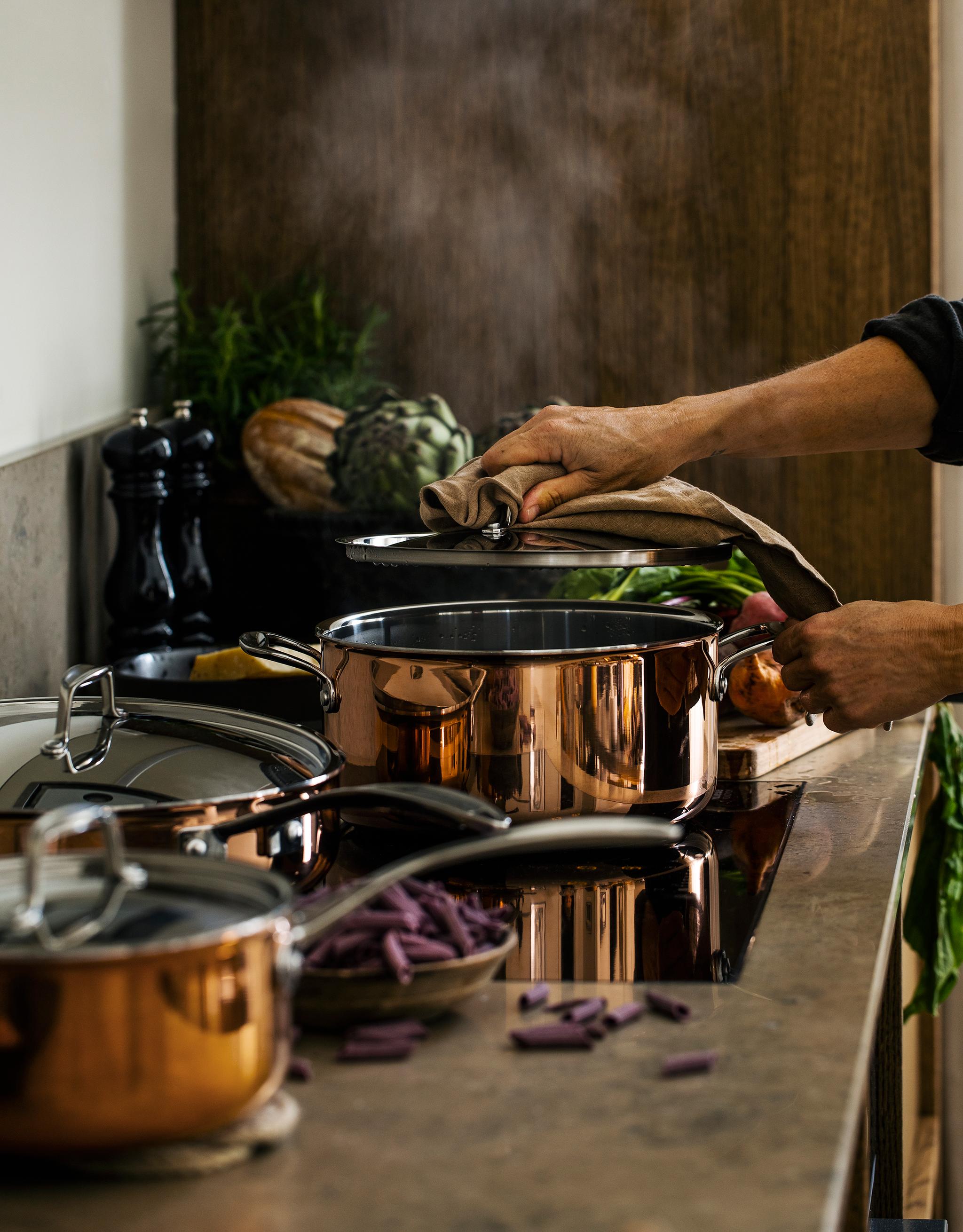 En person lagar mat i kastruller och grytor i koppar