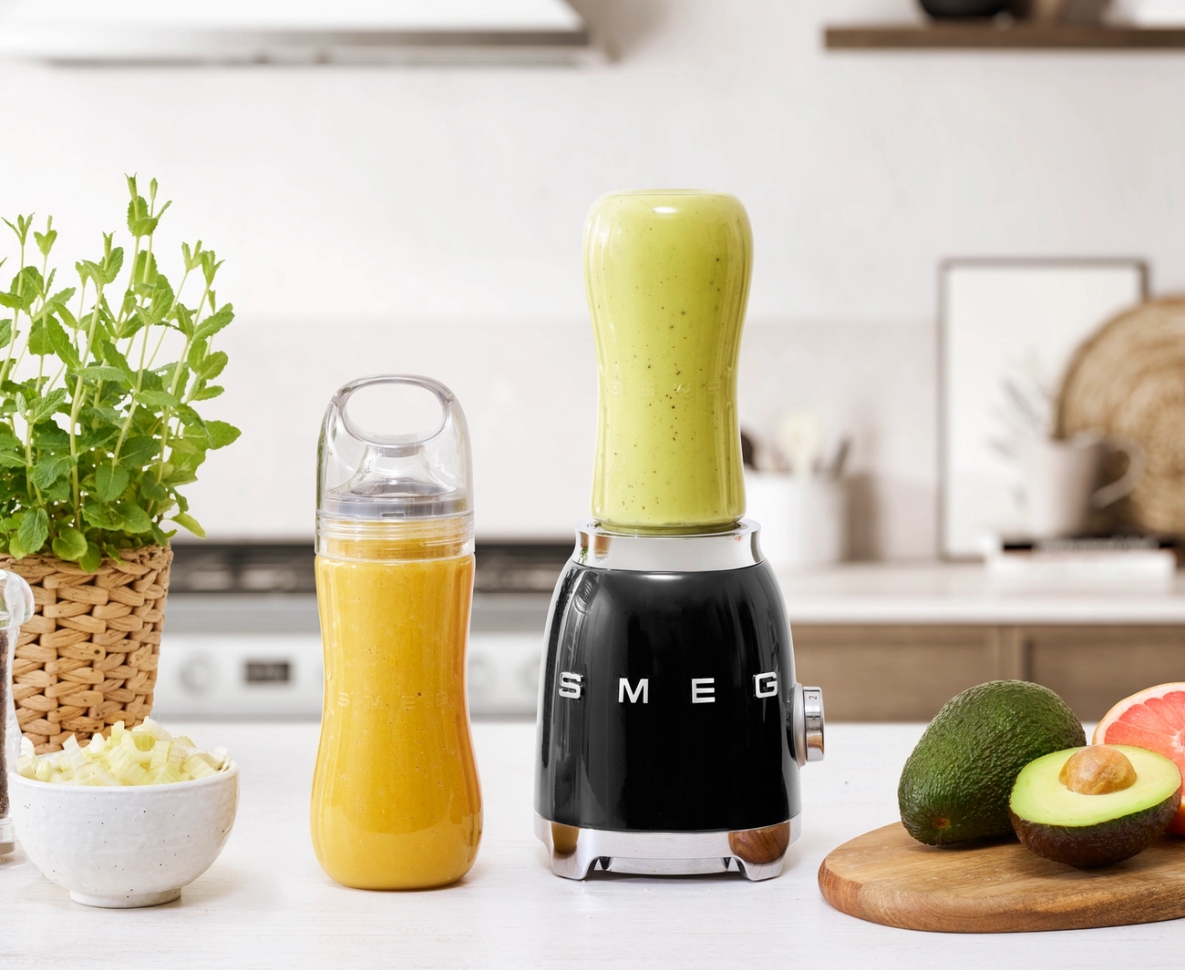 Pieni tehosekoitin tuotemerkiltä smeg täynnä smoothieta ja pöydällä hedelmiä ja vihanneksia