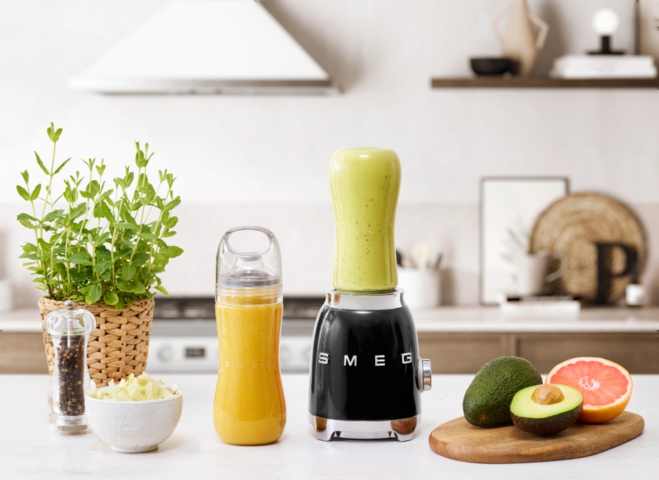 Pieni tehosekoitin tuotemerkiltä smeg täynnä smoothieta ja pöydällä hedelmiä ja vihanneksia