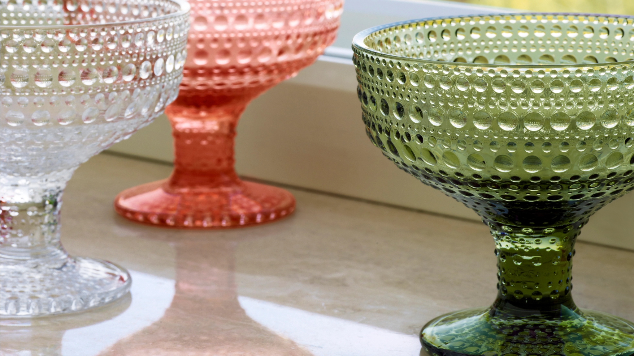 Skål på fot i glas med bubblig textur – tre färger: grönt, rosa och klart, placerade på en fönsterbräda