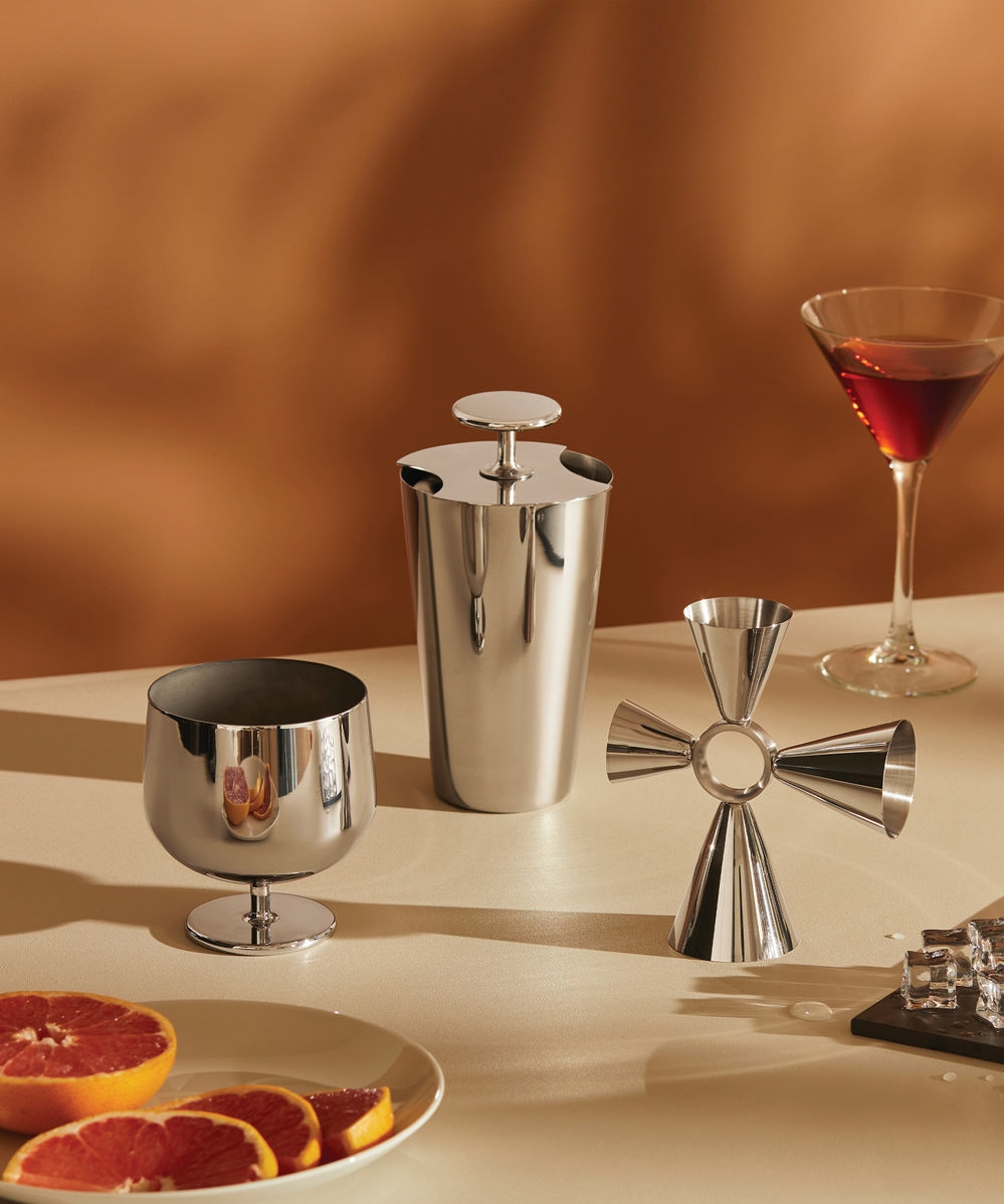 Ruostumattomasta teräksestä valmistetut cocktailvälineet, martini ja greippiviipaleita pöydällä.