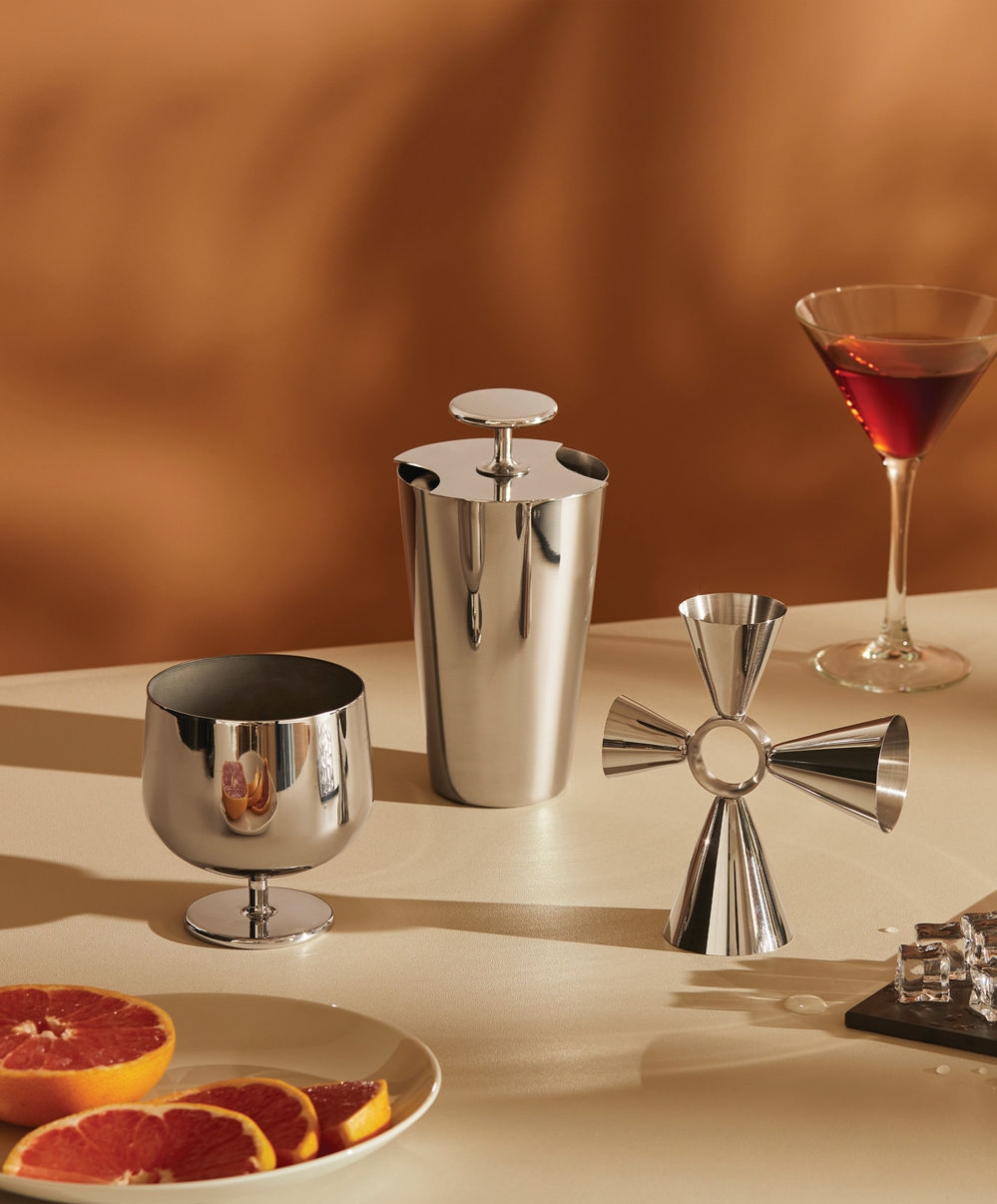 Cocktailverktøy i rustfritt stål, en martini og grapefruktskiver på et bord.