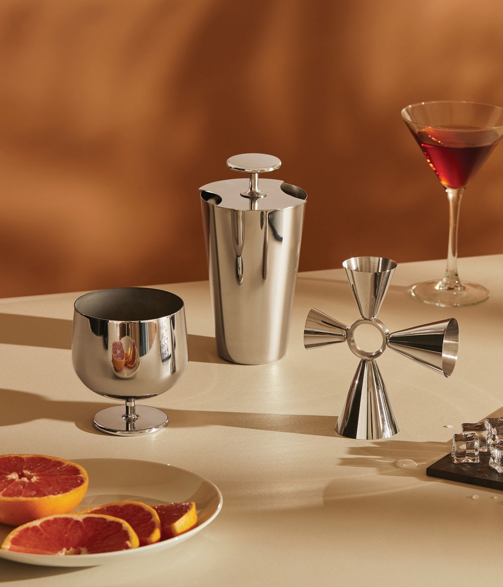 Cocktailverktyg i rostfritt stål, en martini och grapefruktskivor på ett bord.