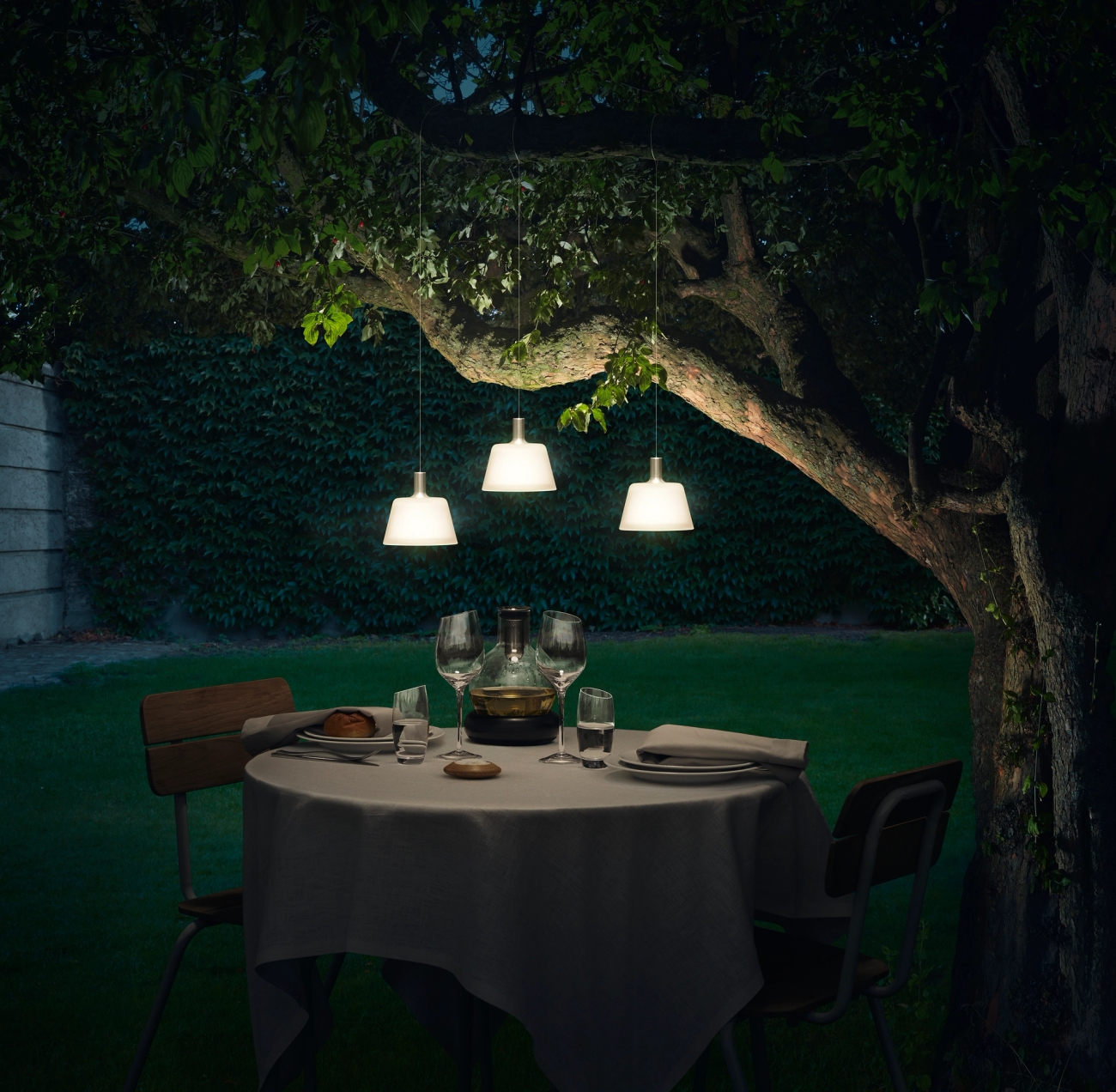 Solcellelamper i hagen som henger i et tre og lyser opp et bord