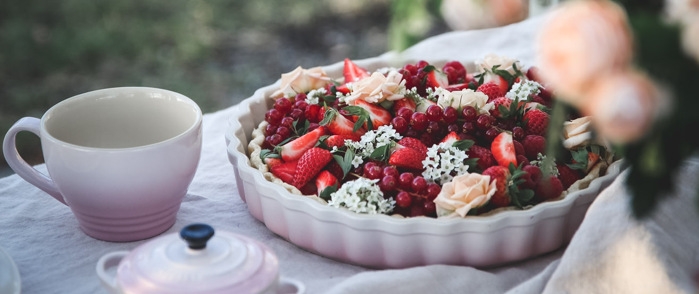 Pajformar, le creuset i ljusrosa med bakat paj med jordgubbar, röda vinbär och blommor