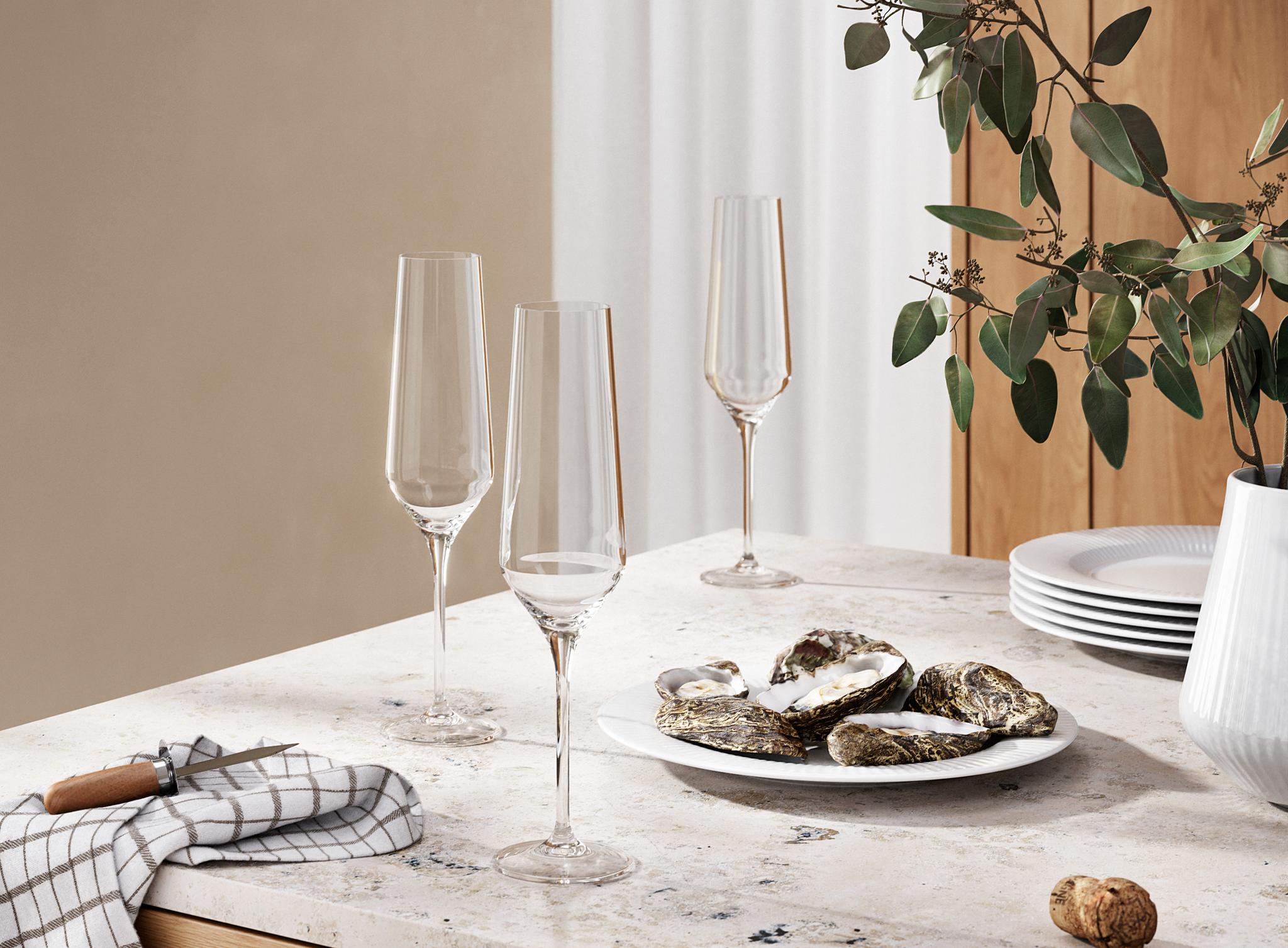 Moderni keittiön tiski, jolla on ostereita, samppanjalasillisia, ruudullinen pyyhe ja kasvi puisten kaappien yläpuolella.