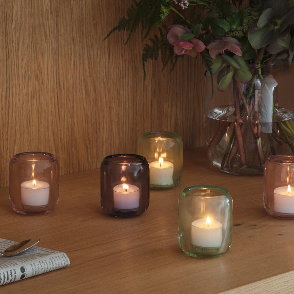 Viisi palavaa teekynttilää värillisissä lasikuvuissa puupinnalla, ja maljakko täynnä kukkia.