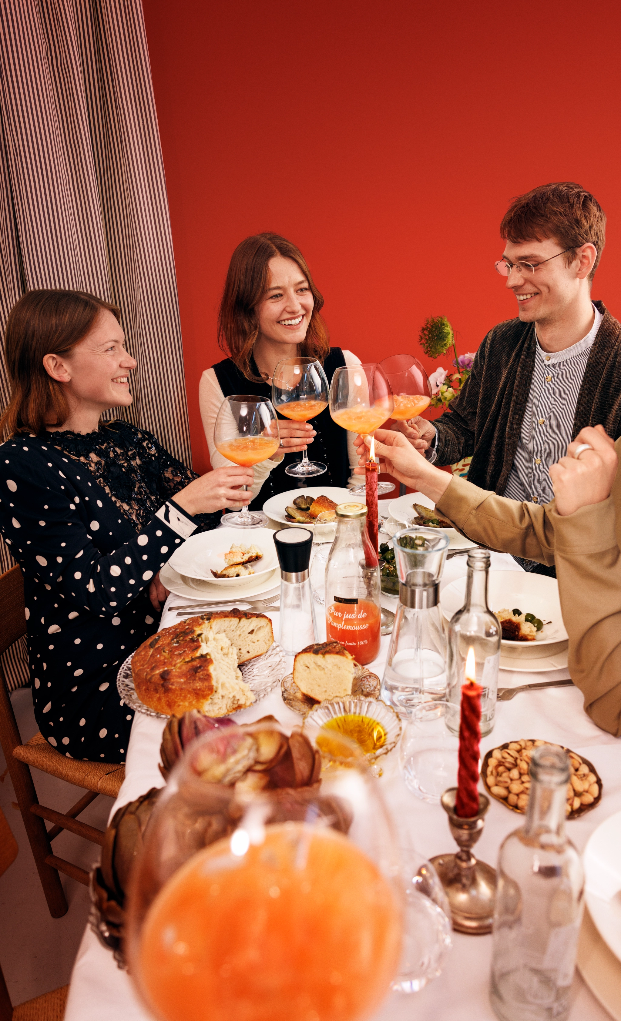 Vänner skålar med orange drinkar under en festlig middag vid ett dukat bord.