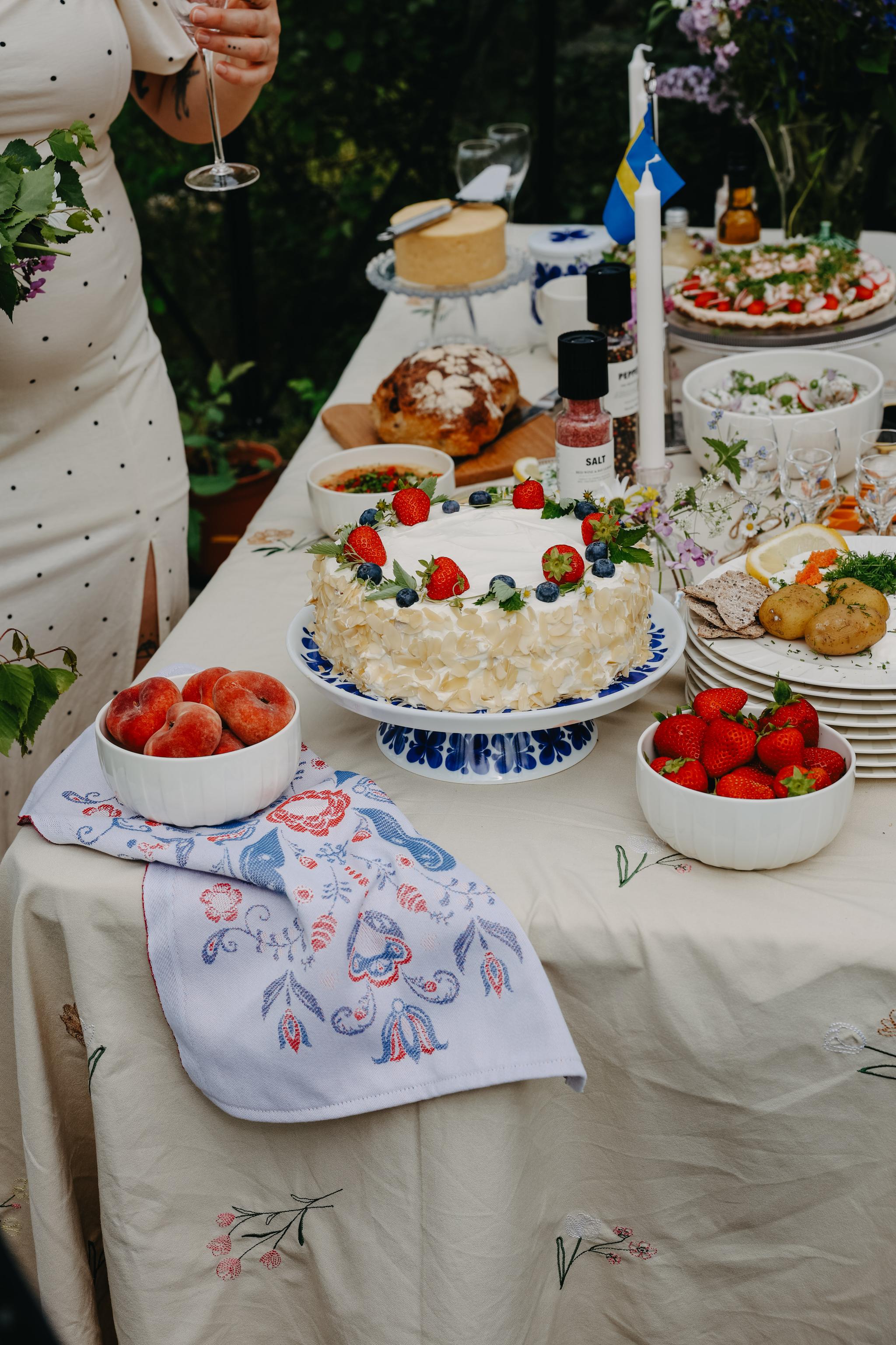 Somrig svensk festdukning utomhus med jordgubbstårta, färska bär och traditionella rätter på ett vackert dekorerat bord.