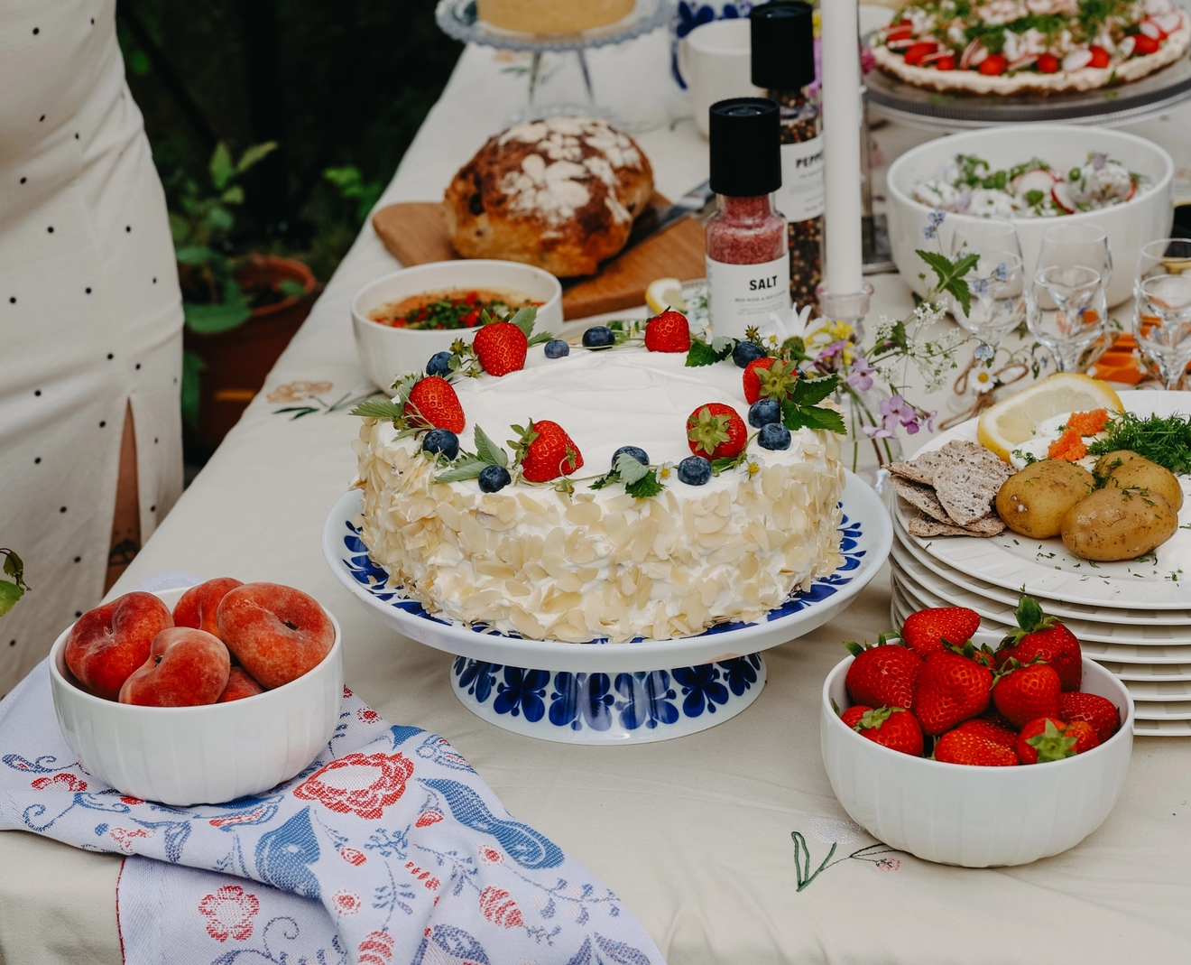 Somrig svensk festdukning utomhus med jordgubbstårta, färska bär och traditionella rätter på ett vackert dekorerat bord.